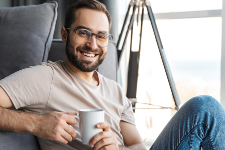 Mann lächelt beim Kaffee trinken in seiner Wohnung zufrieden in die Kamera